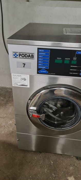 Begagnad Podab industritvättmaskin i ett tvättrum med synligt avloppsanslutning.