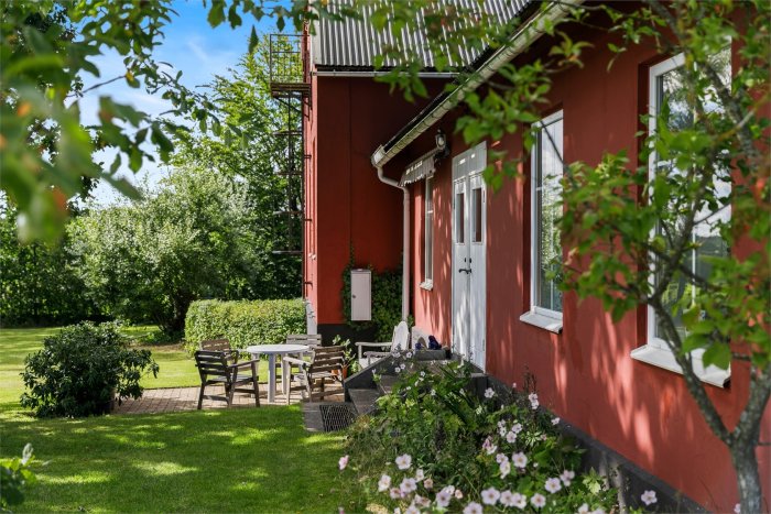 Rödmålat hus med två taknivåer och trädgård, potentiellt före ett planerat taklyft och renovation.