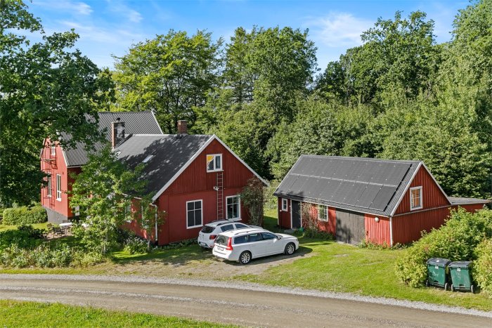 Lantligt rött hus med två våningar och intilliggande lägre byggnad med takfönster, omgiven av grönska.