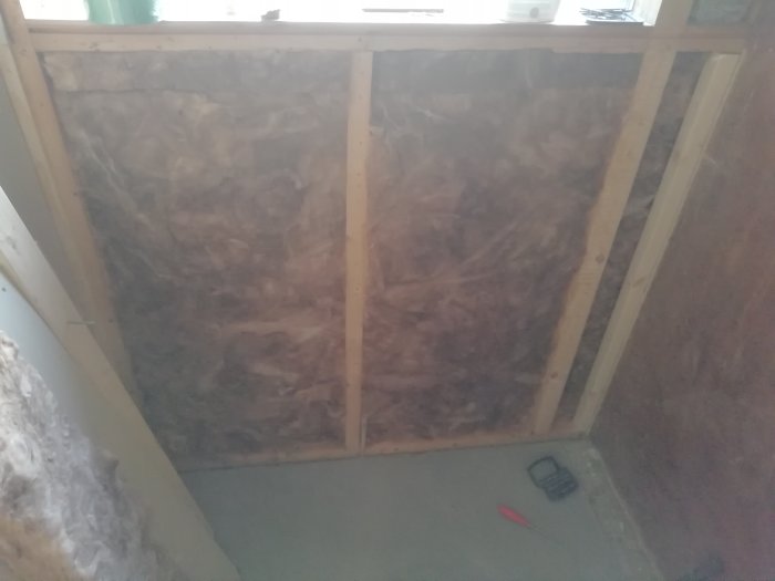 Renovering av vägg med ny ångspärr monterad över gammal spånskiva och isolering, verktyg på golvet.