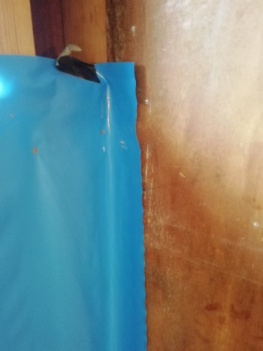 En ny blå ångspärr vikt över en gammal brungul spånskiva vid en väggregel under renovering.