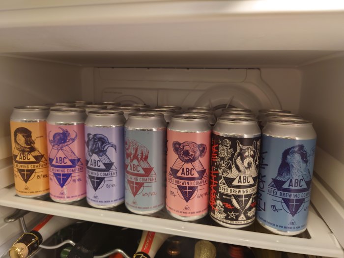 Rad med ölburkar från ABC Brewing Company i olika färger med djurgrafik i ett kylskåp.