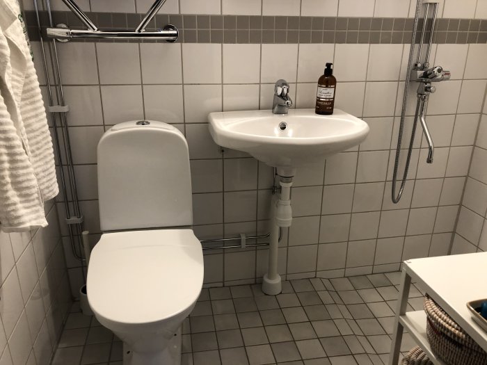 Ett litet badrum med toalett och ett tvättställ med synliga rör som går ner i golvavloppet.
