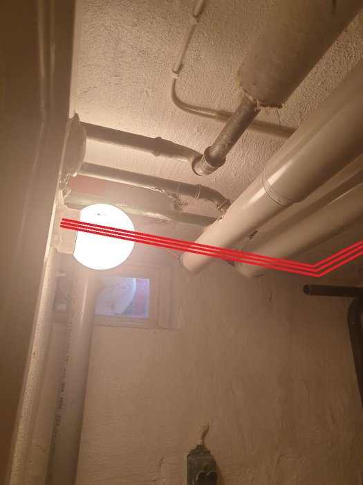 Rörinstallation i källare med markerade röda linjer som visar planerad ny dragning längs väggen.