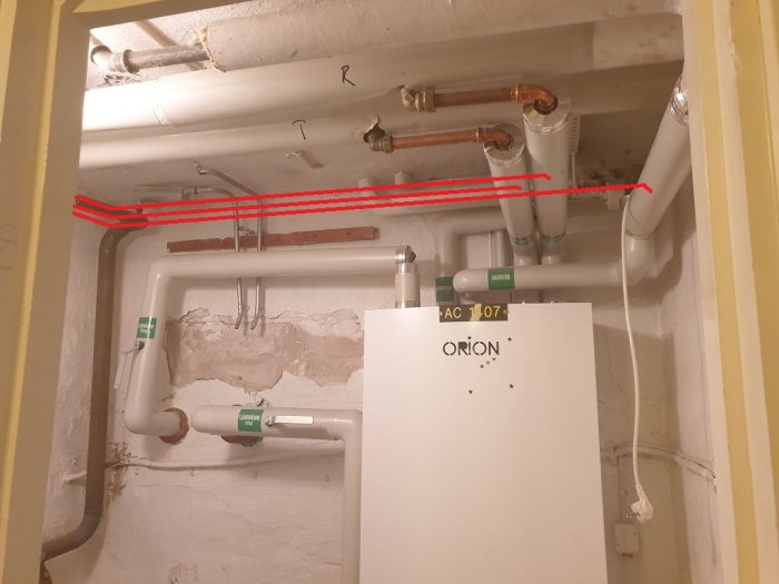 Rörinstallation i källare med red markerad önskad framtida rördragning längs väggen och befintliga rör i taket och väggen.