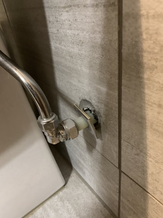 En vägganslutning av ett rör bakom WC där fixeringen lossnat och exponerat området bakom kaklet.