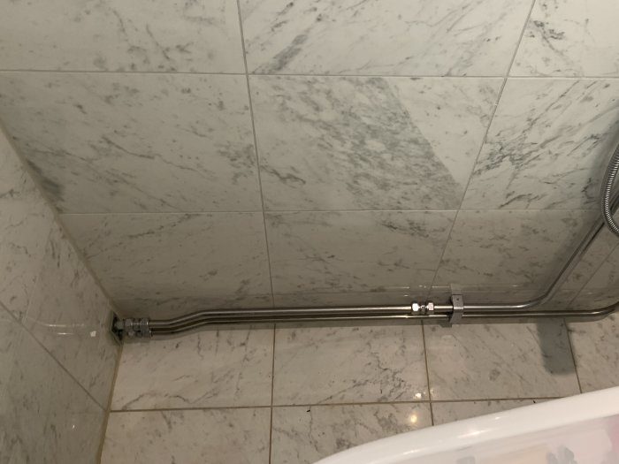 Vattenledningsrör löper längs golv och vägg i ett hörn bakom en WC, utan synligt avstånd mellan rör och vägg.