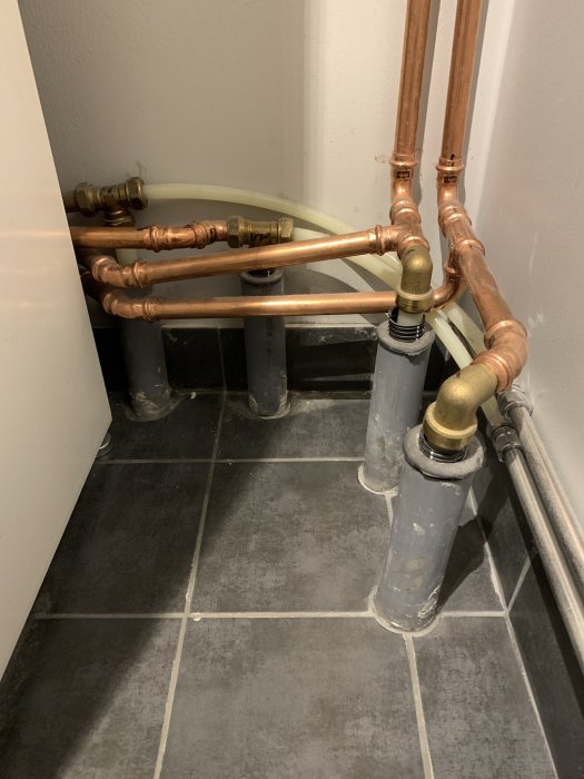Rörinstallationer med kopparledningar och plastslangar bakom WC i badrum, avståndsproblem noteras.