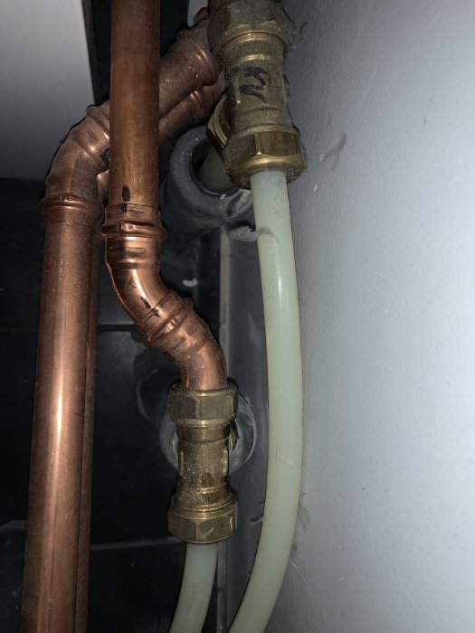 Bild på VVS-installation med kopparledningar och plastslangar nära en grå vägg, potentiellt felaktigt monterade.