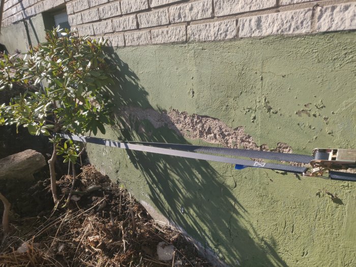 Horisontell spricka i en grundmur med putssläpp, mätt med ett spännband.