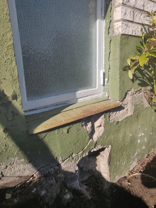 Horisontell spricka i grundmur nära fönster med putssläpp och fuktskador.