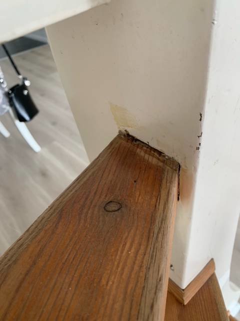Sliten trätrappsteg och vit målad sida där färg lossnat och visar tecken på slitage och smuts.