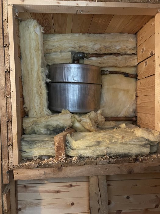 Öppet utrymme i en vägg med isolering och gamla rör som misstänks vara del av ett äldre oljesystem under renovering.