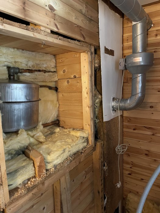 Rivet utrymme med synlig isolering och metallrör, misstänkt del av gammalt oljesystem.