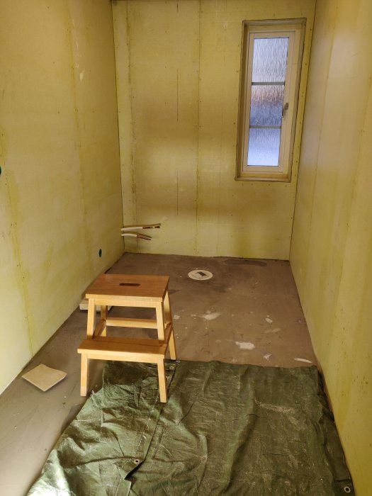 Renoveringsrum med gula primade väggar och oskyddat golv före tätskiksapplicering.