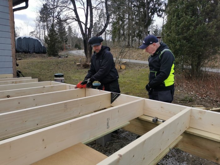 Två personer bygger ett träramverk för ett byggprojekt utomhus.