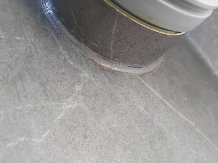 Nyligen installerad matta i badrum med synlig skarv och silikon runt avloppsrör, tejp rester kvar.