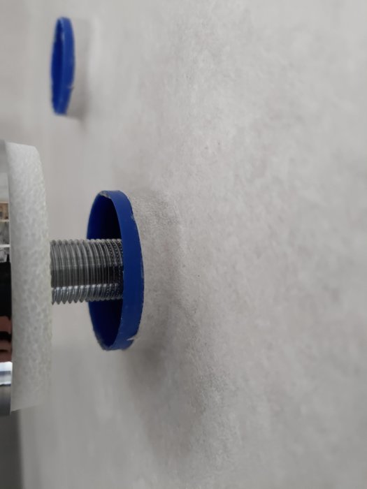 Närbild på skarvad matta kring blå skyddsringar på duschblandarens rörstick i badrum.