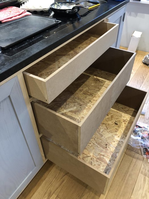 Öppna kökslådor av skivmaterial i en pågående renovering, med en stekpanna ovanpå.