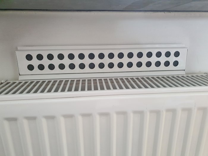 Inluftsgaller ovanför en vit radiator i en lägenhet med synliga filter som användaren söker ersättning för.