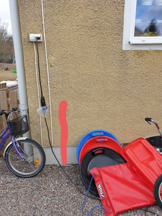 Husvägg med rött streck där installation är planerad, rör längs väggen, cykel och barnvagn i förgrunden.