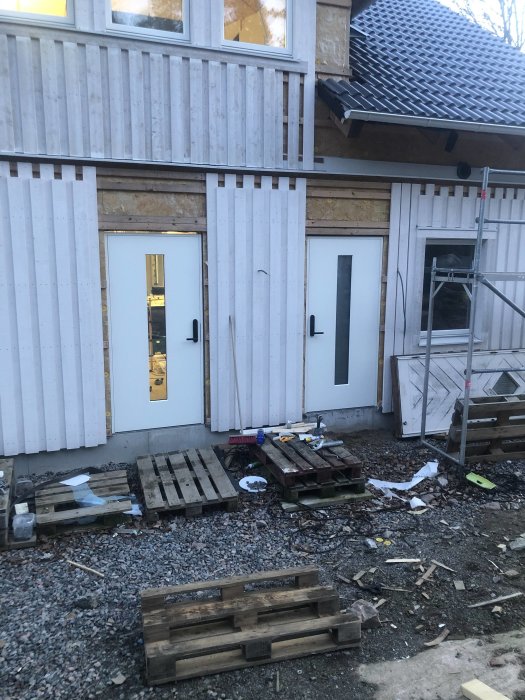 Nyinstallerade ytterdörrar med Yale doorman på ett bygge med panel och byggmaterial runtomkring.