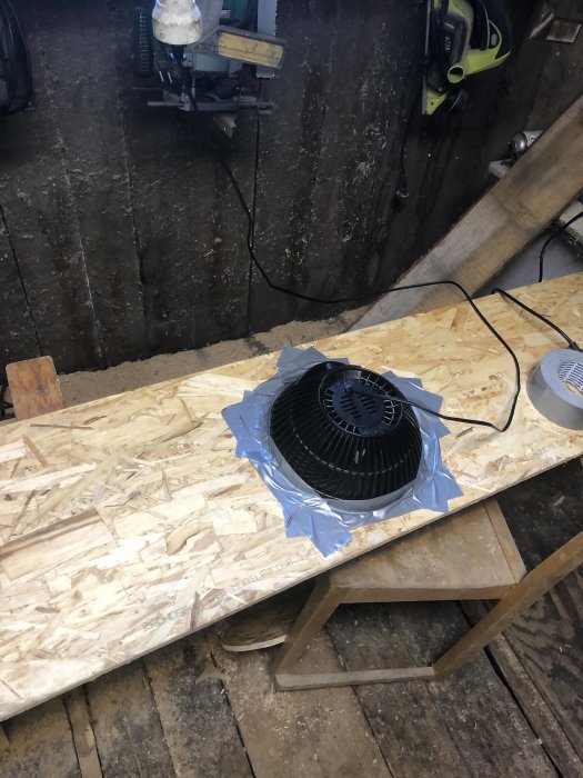 Nyinstallerad fläkt på OSB-skiva med ventilstängningar, omgiven av verktyg och byggmaterial.