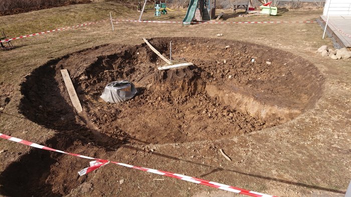 En stor grävd grop för dräneringsbrunn med avgränsande röd-vit varningstejp runtomkring.