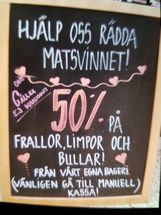 Svart tavla med "Hjälp oss rädda matsvinnet! 50% på frallor, limpor och bullar!" felstavat som "matsvinnet".