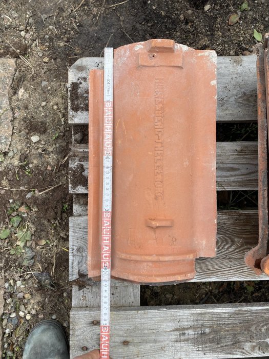 Tegelpanna från Minnesberg Trelleborg mätande ca 40 cm, placerad på träpall med måttband bredvid.