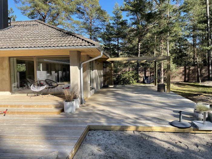 Nyligen byggd pergola inspirerad av Wingårdhs-hus ovanför en träterrass med enhetliga dimensioner omgiven av tallar.