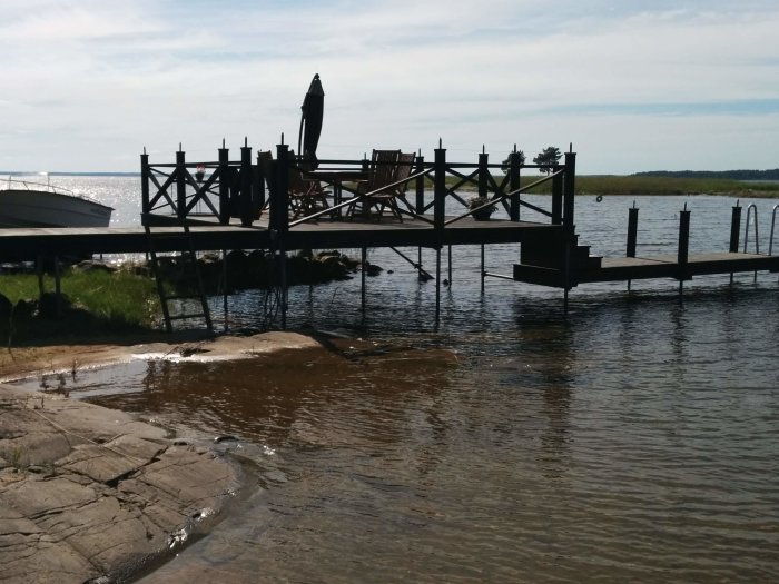 Stabil träbrygga på galvade stålrör vid sjö med förebyggande anordningar mot fågelsittning.