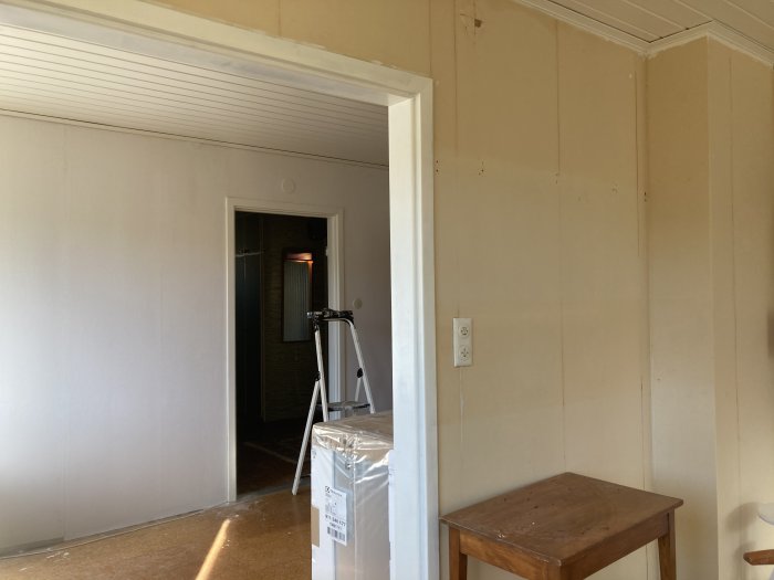 Vägg med masonitskivor och en dörröppning, föreslagen breddningspunkt markerad, i ett rum under renovering.