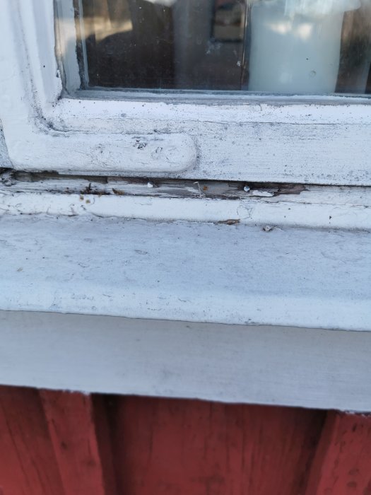 Skadad nederkant på en vitmålad fönsterkarm på ett äldre hus, med sprickor och flagande färg.