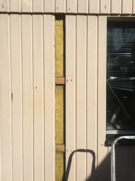Vägg med borttagen planka som visar gul isolering och husets innerskikt.