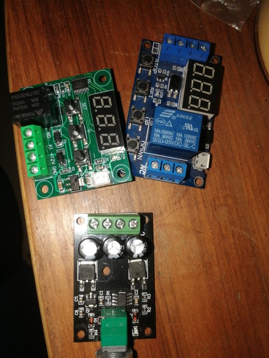 Tre olika kretskort med elektroniska komponenter på ett träbord.