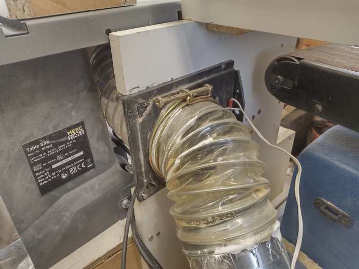Dammsugarslang kopplad till träbearbetningsmaskin med synliga mikrobrytare och elektrisk utrustning.