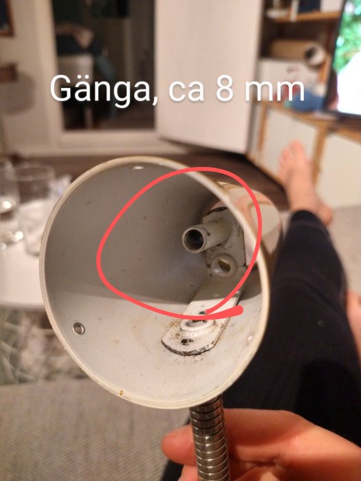 Närbild av en gammal vit lampskärm med en gängad anslutning på ca 8 mm riktad mot kameran, i ett hemmiljö.