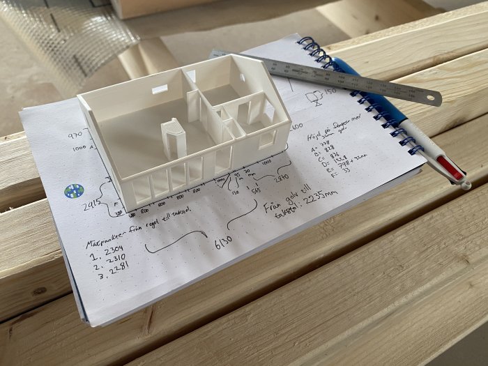 3D-printad modell av ett hus på skissblock med handritade byggplaner och en linjal.