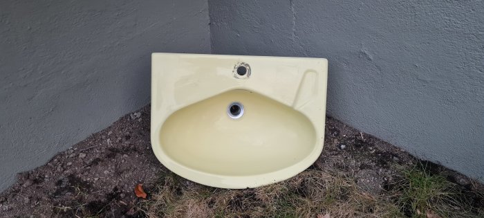 Retro gult hörnhandfat som ligger mot en grå vägg utomhus, redo att skänkas bort.