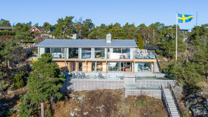 Moderna arkitektritade villa på Smådalarö med stora fönster, terrass och svensk flagga.