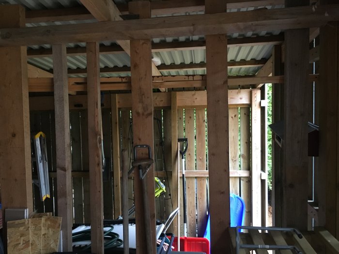 Interiör av ett uthus med trästomme, verktyg och plåttak, potentiell bastuombyggnad.