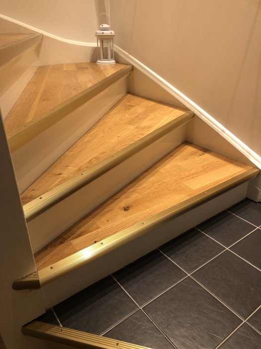Renoverad trappa med nya steg av parkettgolv och vitmålade sidor, belyst stegkant ovanför klinkergolv.