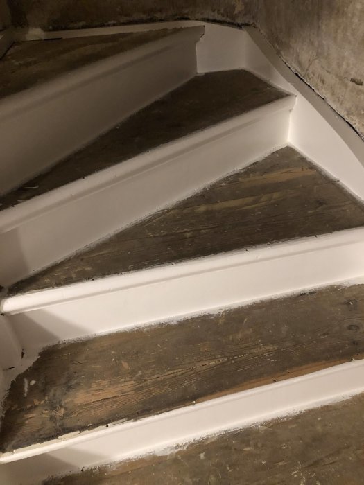 Halvfärdigt trapprenoveringsprojekt med pålagda trästeg på vitmålade trappor.