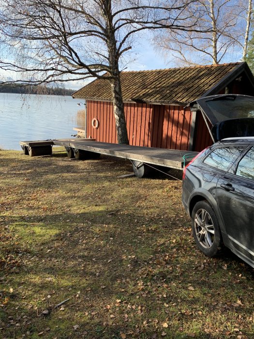 Bild på en bil som drar en brygga med extra tunna närmast bilen vid en sjö med röd stuga och träd i bakgrunden.