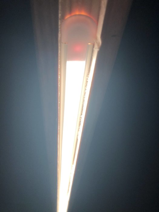 Infälld LED-slinga i träregel, sedd underifrån, med stark ljusstråle och skuggor.