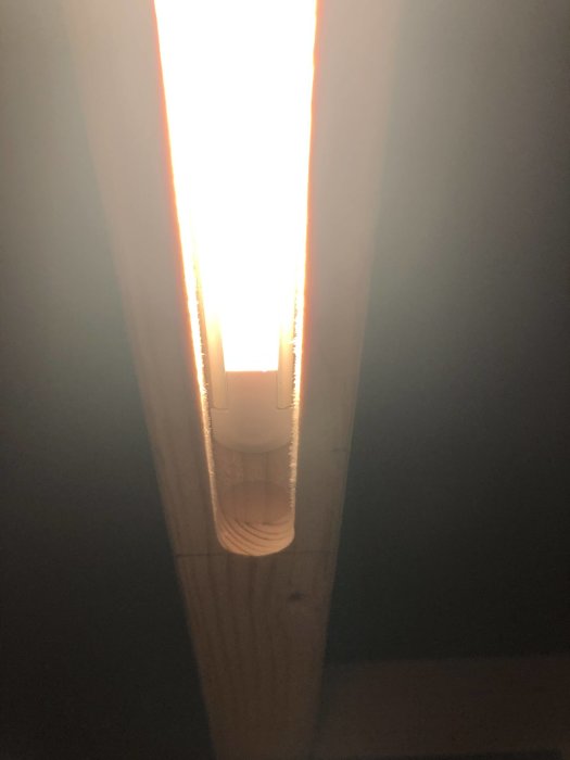 Infälld LED-slinga i träregel lyser upp, syns underifrån med starkt ljus och tjock sladd.