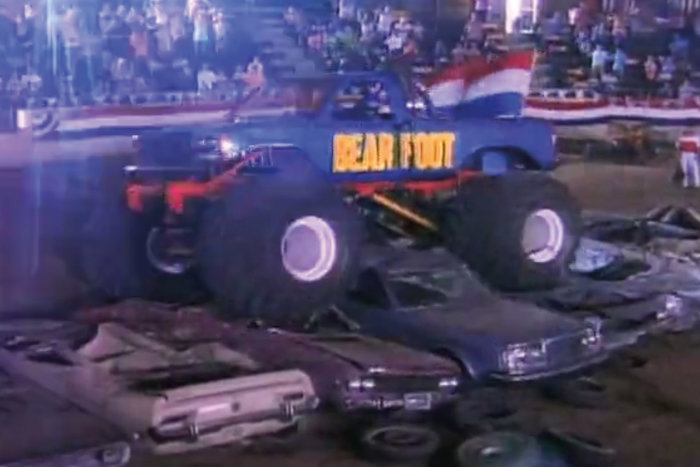 Monstertruck med texten "Bear Foot" kör över krossade bilar under en uppvisning.