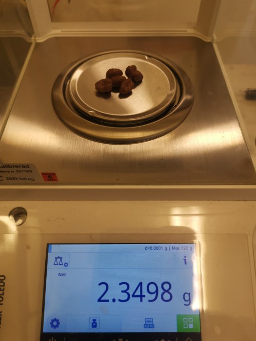 Kaffebönor vägs på en digitalvåg som visar 2.3498 gram.