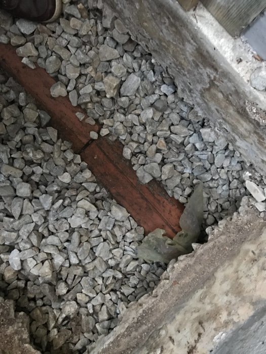 Öppning i betong med synlig keramikrör-dränering och grus, en del av ett krypgrundssystem.